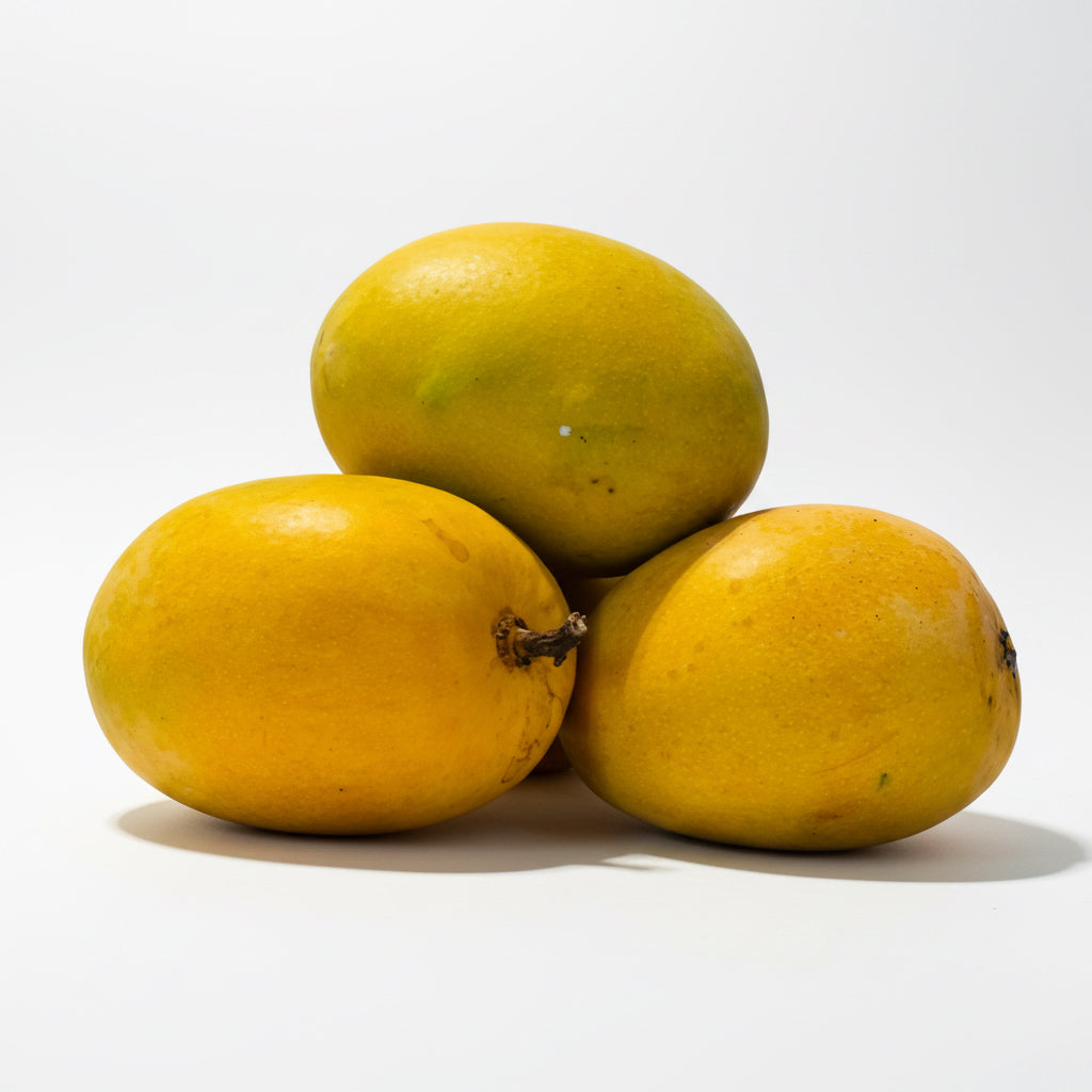 Three yellow mangoes stacked on a light surface with a light blue background